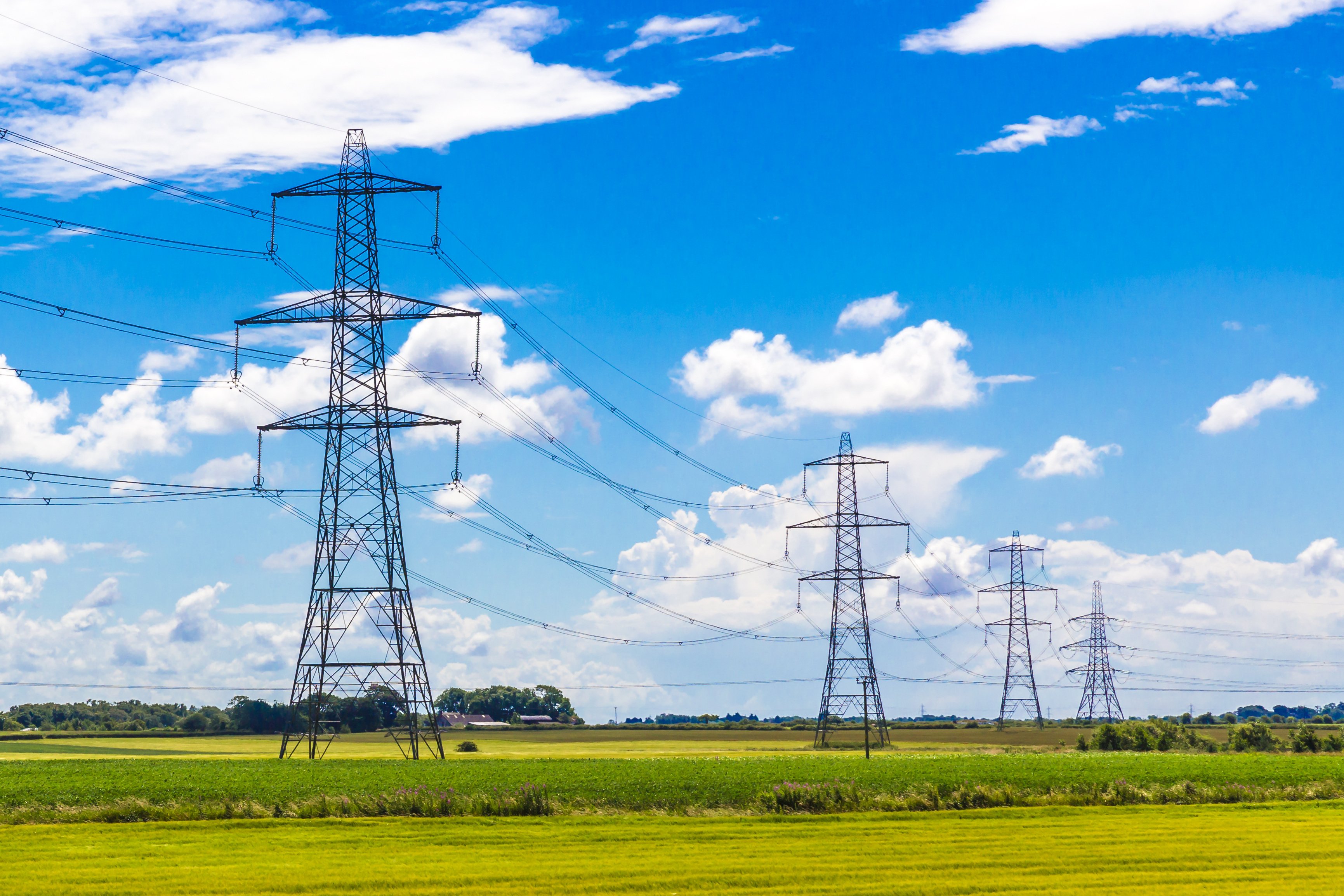 Electricity pylons connected by cables in a green field with blue sky.