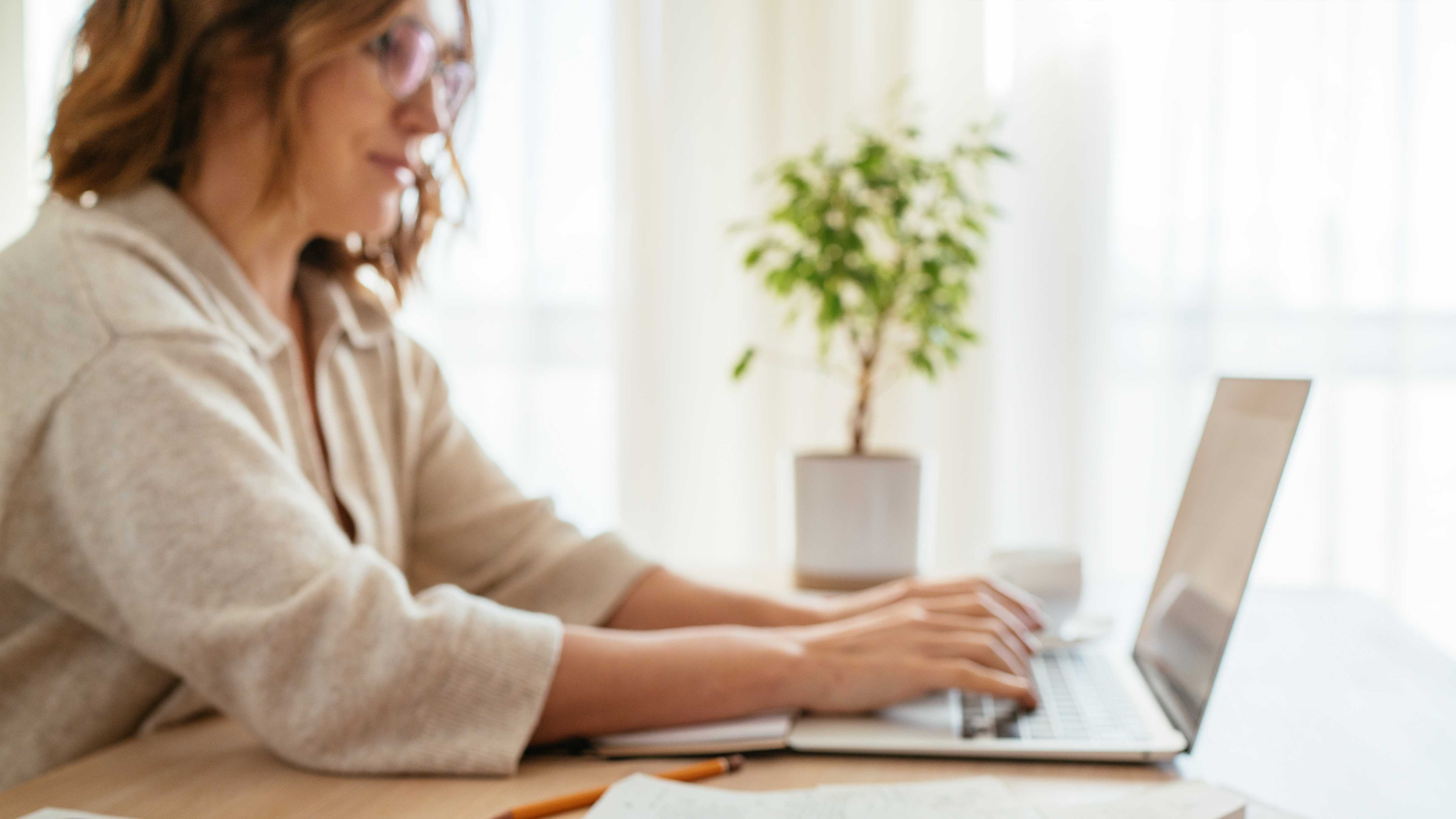 A woman typing on a laptop with a calculator and business energy bills.
