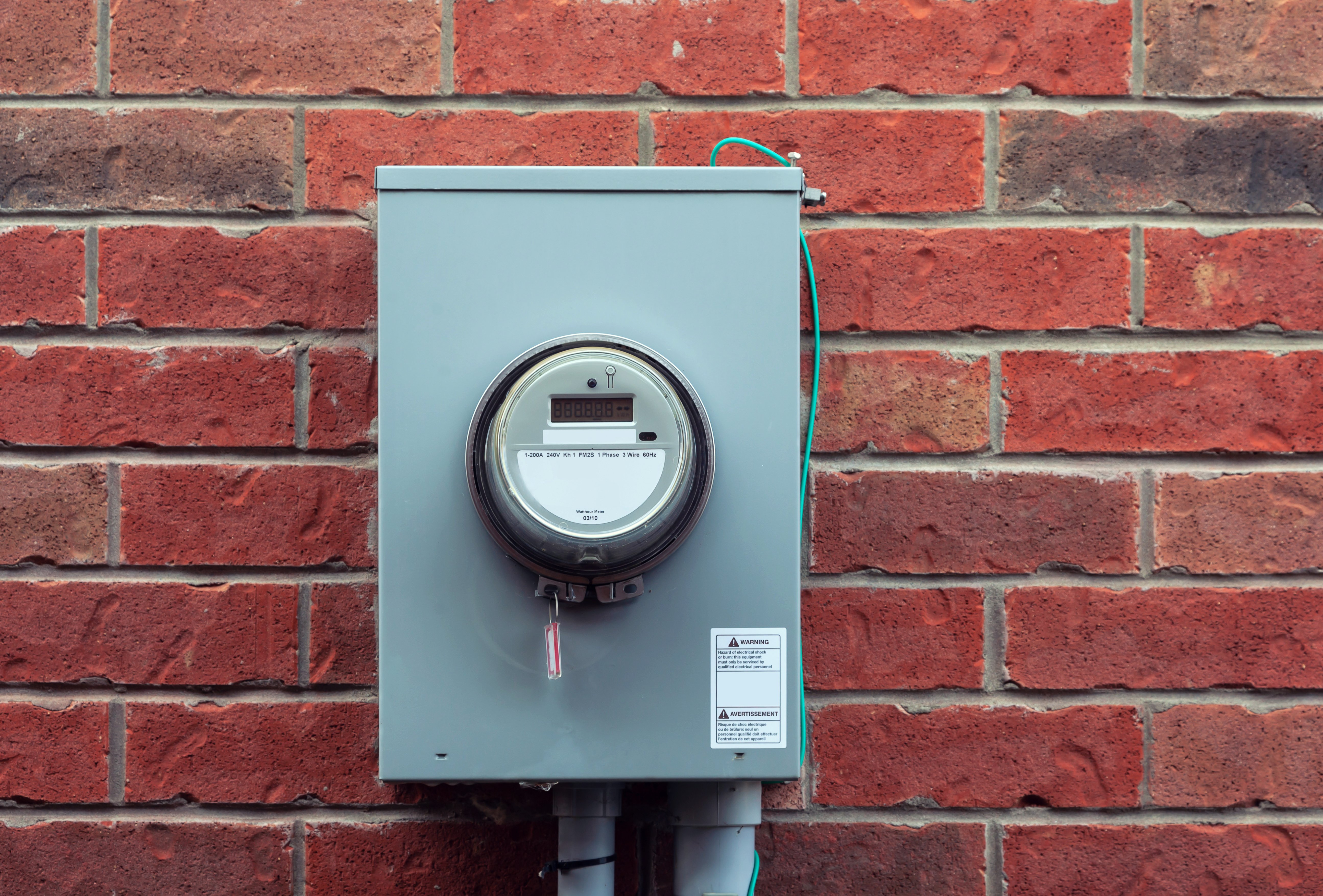 An electricity meter on the red brick wall of a building.