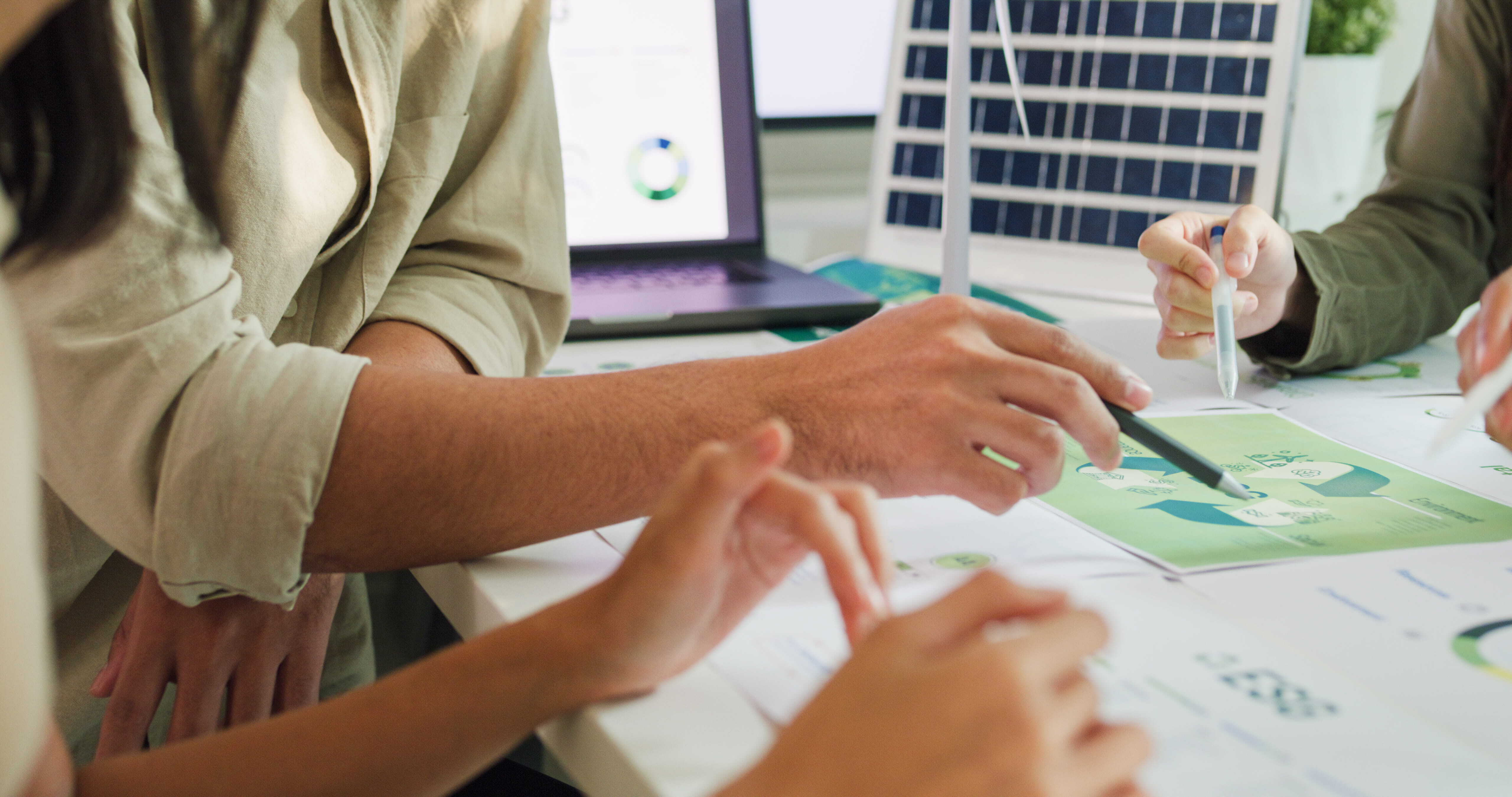 Close-up of three people pointing at plans on a desk.