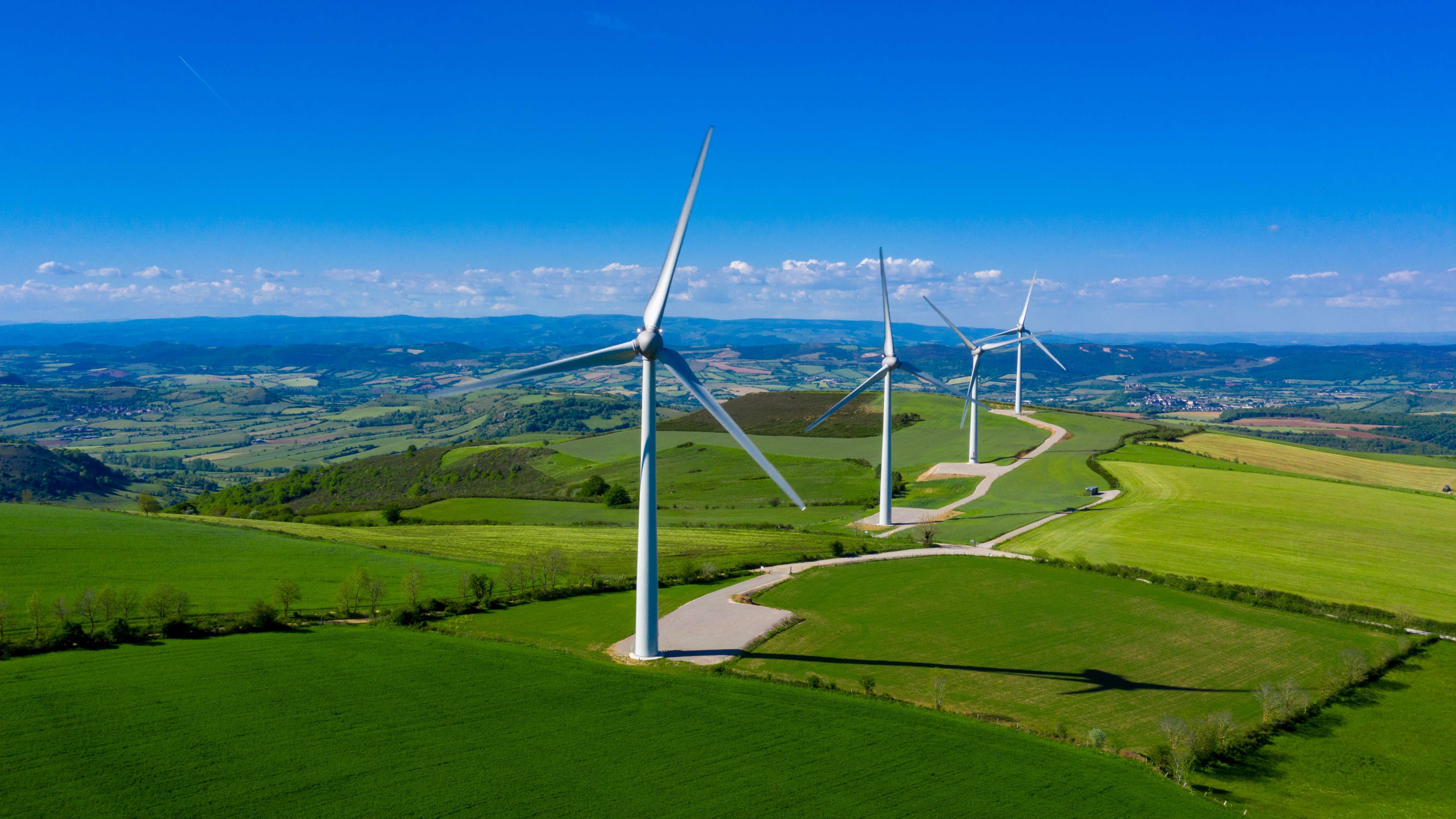 General view of wind turbines in green fields with blue sky.