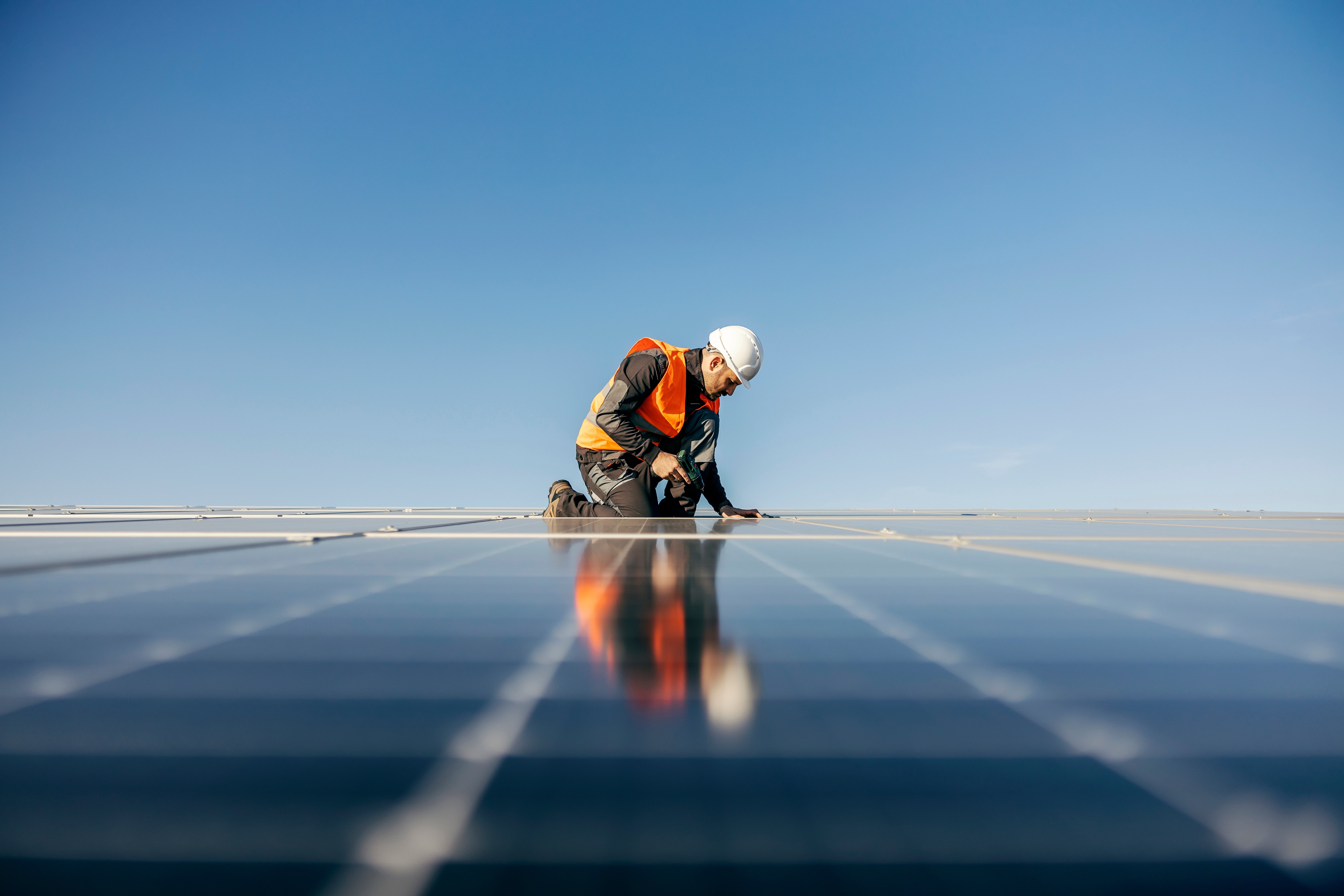 A man in a high-vis jacket installing solar panels on a roof.